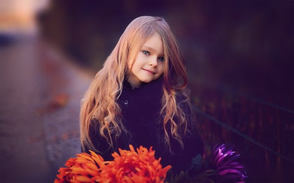 Dziewczynka z długimi włosami stoi z kwiatami na chodniku